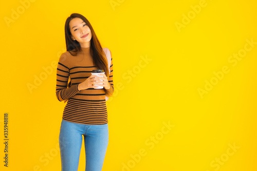 Portrait beautiful young asian woman with bagpack and coffee cup in her hand on yellow background
