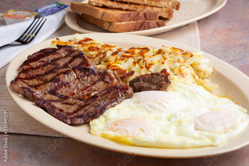 Valokuva A view of a breakfast plate featuring over easy eggs, a steak cut, hash browns and toast, in a restaurant or kitchen setting