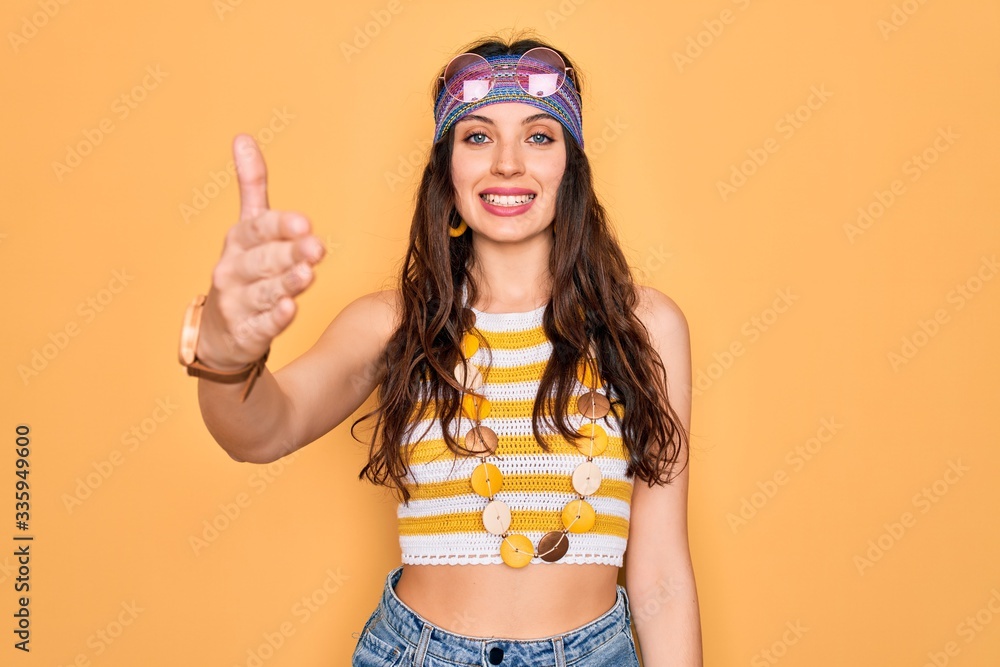 Young beautiful hippie woman with blue eyes wearing accesories and sunnglasses smiling friendly offering handshake as greeting and welcoming. Successful business. Young beautiful hippie woman with blue eyes wearing accesories and sunnglasses smiling friendly offering handshake as greeting and welcoming. Successful business.