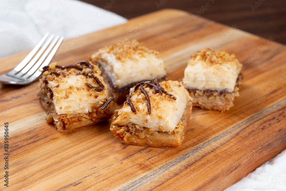 A view of pieces of baklava with chocolate syrup on a wooden board, in a restaurant or kitchen setting.