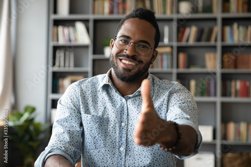 Headshot portrait of smiling african American young male employer stretch hand welcoming newcomer at workplace, happy biracial man boss in glasses meeting job candidate, employment concept photo