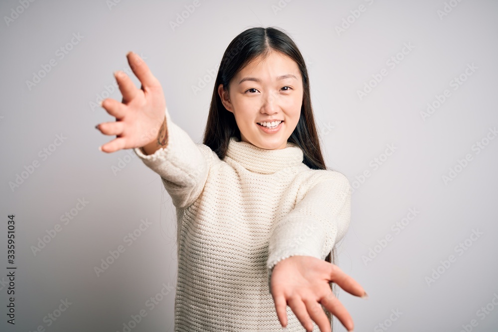 Young beautiful asian woman wearing casual sweater standing over isolated background looking at the camera smiling with open arms for hug. Cheerful expression embracing happiness. Young beautiful asian woman wearing casual sweater standing over isolated background looking at the camera smiling with open arms for hug. Cheerful expression embracing happiness.