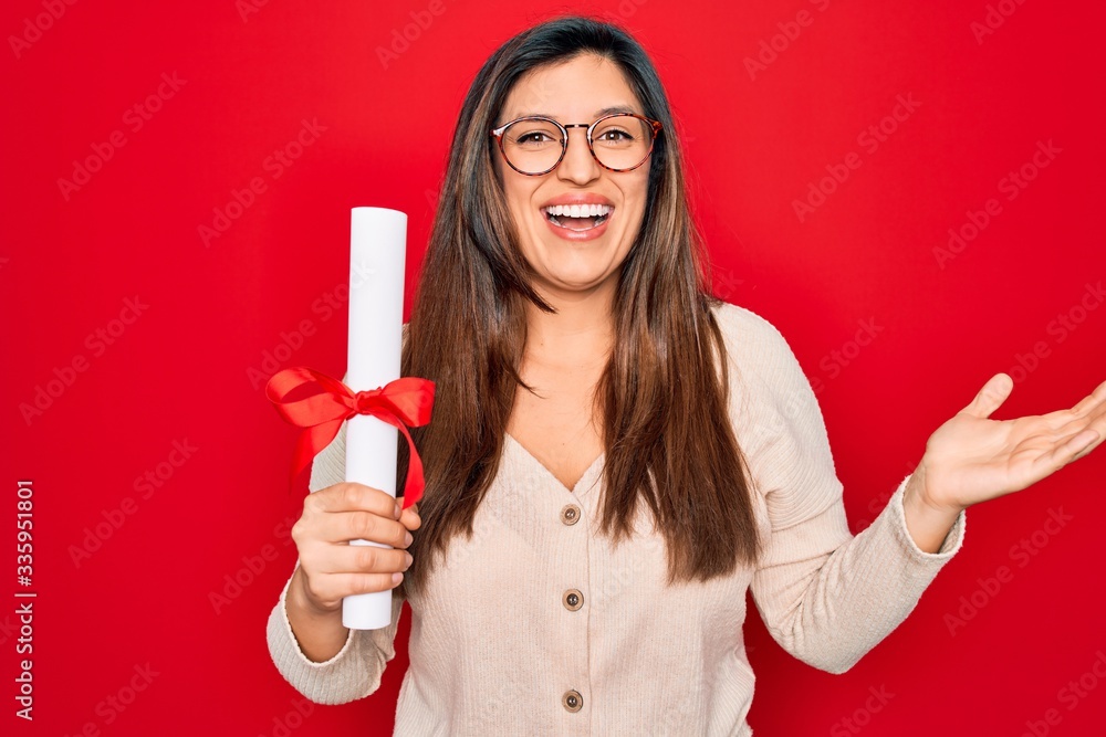 Young hispanic smart woman wearing glasses holding university degree over red background very happy and excited, winner expression celebrating victory screaming with big smile and raised hands Young hispanic smart woman wearing glasses holding university degree over red background very happy and excited, winner expression celebrating victory screaming with big smile and raised hands