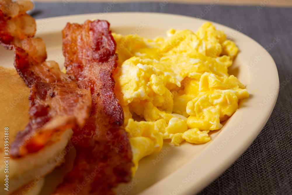 A closeup view of a breakfast plate, featuring scrambled eggs and bacon, in a restaurant or kitchen setting. A closeup view of a breakfast plate, featuring scrambled eggs and bacon, in a restaurant or kitchen setting.