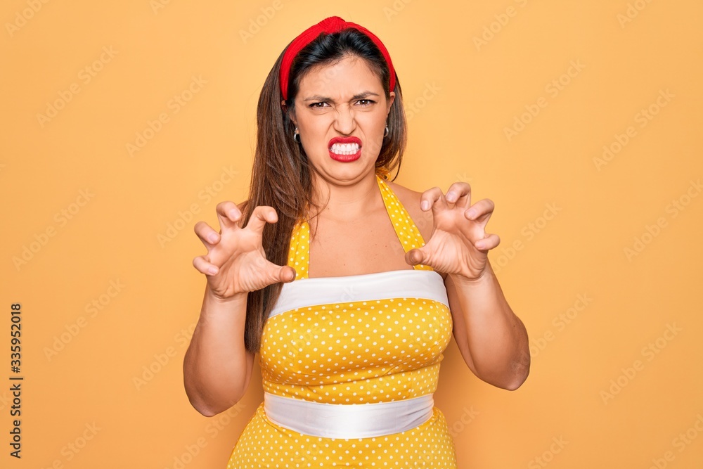Young hispanic pin up woman wearing fashion sexy 50s style over yellow background smiling funny doing claw gesture as cat, aggressive and sexy expression Young hispanic pin up woman wearing fashion sexy 50s style over yellow background smiling funny doing claw gesture as cat, aggressive and sexy expression
