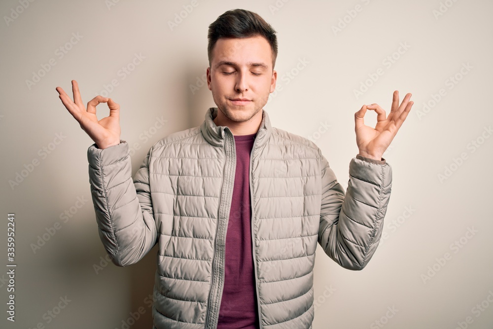 Naklejka premium Young handsome caucasian man wearing casual winter jacket standing over isolated background relax and smiling with eyes closed doing meditation gesture with fingers. Yoga concept.