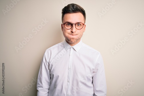 Young handsome business mas wearing glasses and elegant shirt over isolated background puffing cheeks with funny face. Mouth inflated with air, crazy expression.