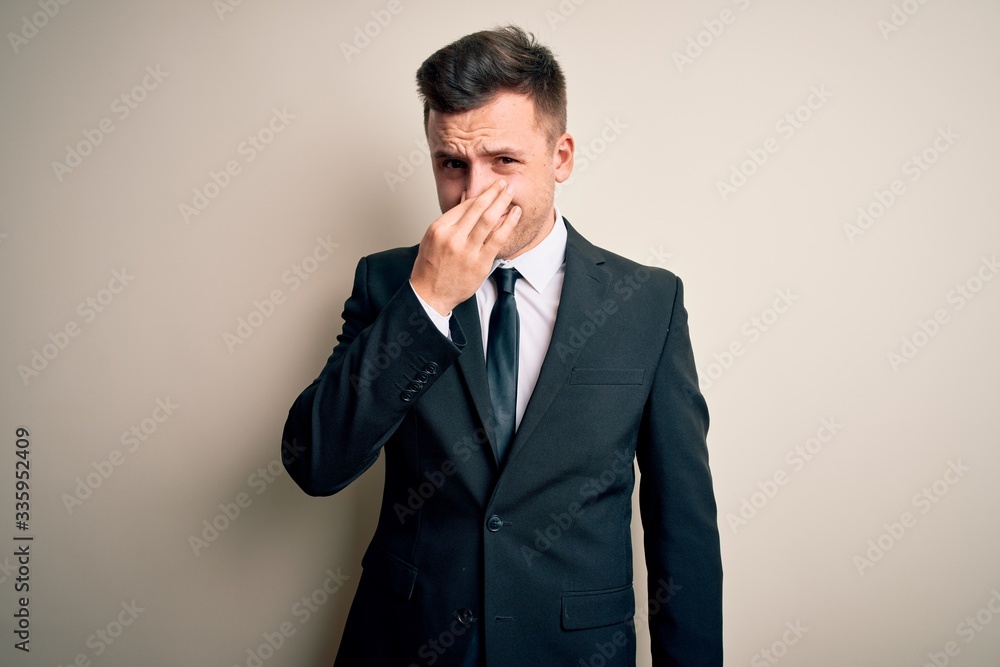 Young handsome business man wearing elegant suit and tie over isolated background smelling something stinky and disgusting, intolerable smell, holding breath with fingers on nose. Bad smell Young handsome business man wearing elegant suit and tie over isolated background smelling something stinky and disgusting, intolerable smell, holding breath with fingers on nose. Bad smell