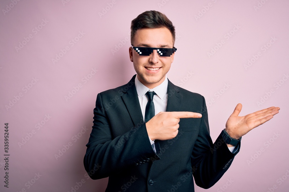 Young handsome caucasian business man wearing funny thug life glasses amazed and smiling to the camera while presenting with hand and pointing with finger. Young handsome caucasian business man wearing funny thug life glasses amazed and smiling to the camera while presenting with hand and pointing with finger.