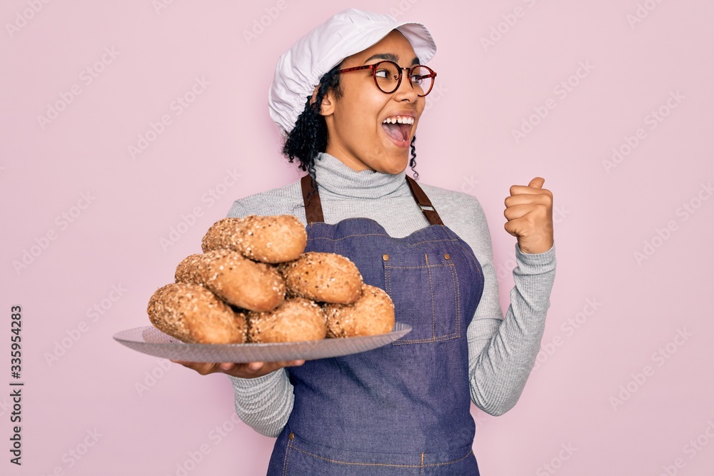 Young african american baker woman wearing apron holding wholemeal bread with cereal pointing and showing with thumb up to the side with happy face smiling Young african american baker woman wearing apron holding wholemeal bread with cereal pointing and showing with thumb up to the side with happy face smiling