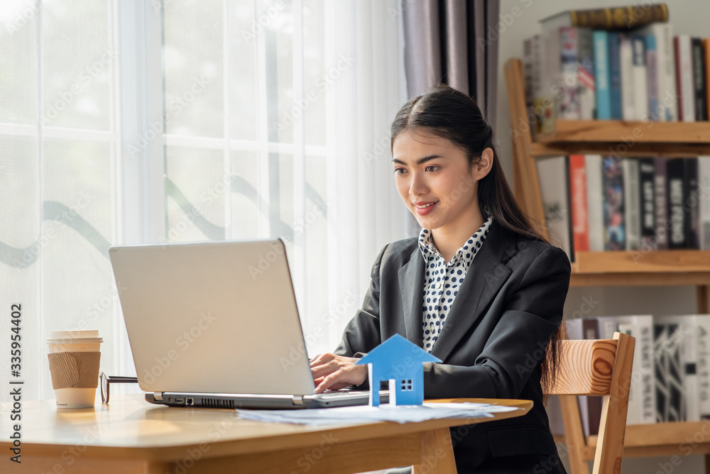 Young Asian business woman working in the office and using her laptop in her office with paper house Young Asian business woman working in the office and using her laptop in her office with paper house