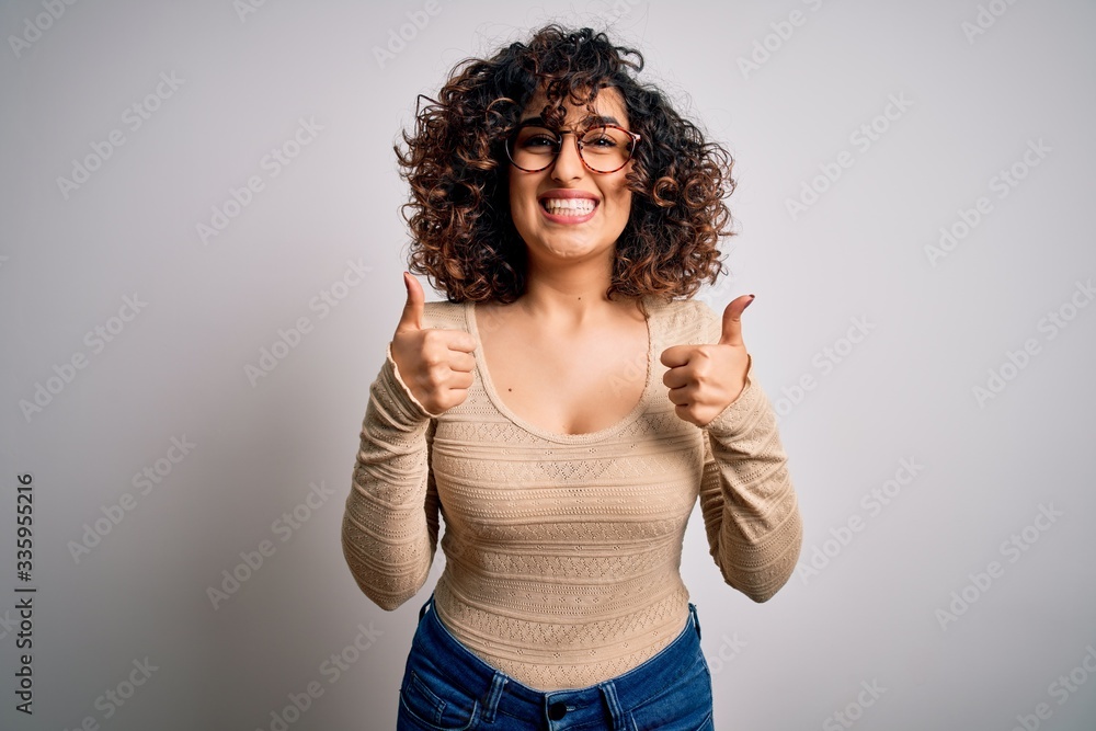 Young beautiful curly arab woman wearing casual t-shirt and glasses over white background success sign doing positive gesture with hand, thumbs up smiling and happy. Cheerful expression and winner Young beautiful curly arab woman wearing casual t-shirt and glasses over white background success sign doing positive gesture with hand, thumbs up smiling and happy. Cheerful expression and winner