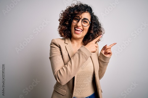 Young curly arab business woman wearing elegant jacket and glasses over white background smiling and looking at the camera pointing with two hands and fingers to the side.