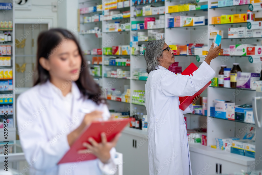 Professional Asian male and female Pharmacist checking medicines and health care product inventory stock on shelf at hospital pharmacy or drugstore. Medical, pharmaceutical and healthcare concept.