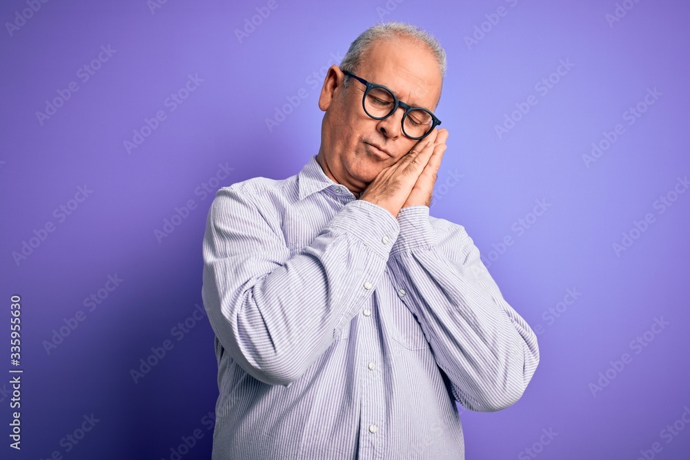Obraz premium Middle age handsome hoary man wearing striped shirt and glasses over purple background sleeping tired dreaming and posing with hands together while smiling with closed eyes.