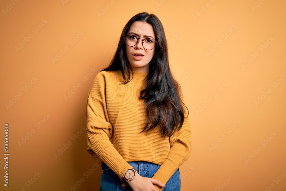 Young brunette woman wearing glasses and casual sweater over yellow isolated background skeptic and nervous, frowning upset because of problem. Negative person. Young brunette woman wearing glasses and casual sweater over yellow isolated background skeptic and nervous, frowning upset because of problem. Negative person.