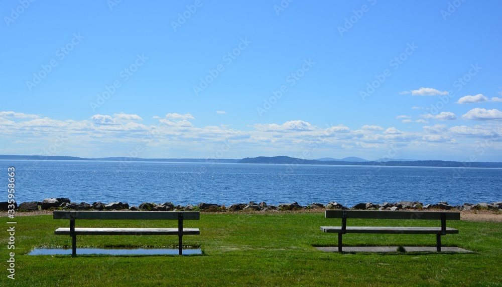 Two benches on a walking path overlooking the Pacific Ocean in Seattle, WA Two benches on a walking path overlooking the Pacific Ocean in Seattle, WA