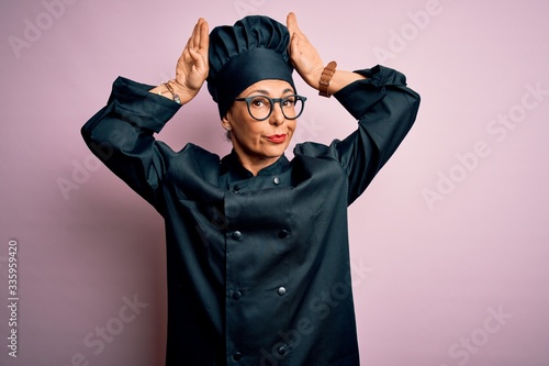 Middle age brunette chef woman wearing cooker uniform and hat over isolated pink background Doing bunny ears gesture with hands palms looking cynical and skeptical. Easter rabbit concept. © Krakenimages.com