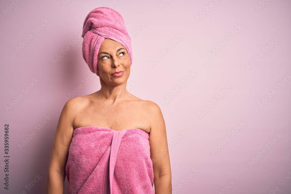 Middle age woman wearing bath towel from beauty body care over pink background smiling looking to the side and staring away thinking. Middle age woman wearing bath towel from beauty body care over pink background smiling looking to the side and staring away thinking.