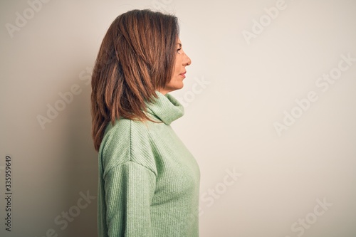 Middle age beautiful woman wearing casual turtleneck sweater over isolated white background looking to side, relax profile pose with natural face with confident smile. © Krakenimages.com