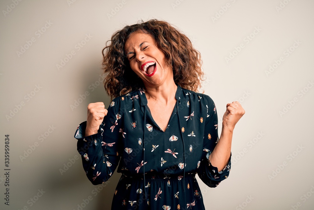 Middle age beautiful woman wearing casual dress standing over isolated white background very happy and excited doing winner gesture with arms raised, smiling and screaming for success. Celebration Middle age beautiful woman wearing casual dress standing over isolated white background very happy and excited doing winner gesture with arms raised, smiling and screaming for success. Celebration