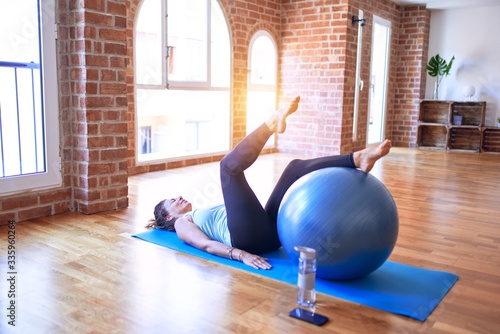 Middle age beautiful sportswoman smiling happy. Doing exercise using fitness ball in a class of yoga at gym