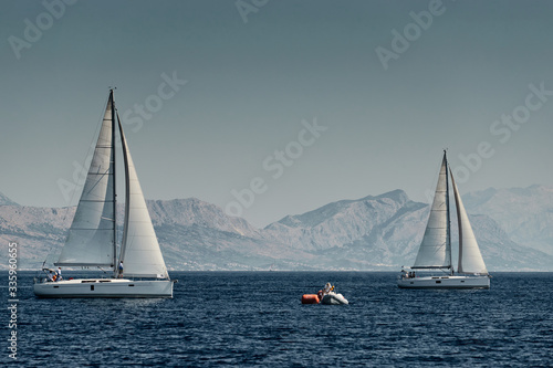 The rubber boat of organizers of a regatta with the judge and balloon of orange color, The race of sailboats, Intense competition, island with windmills are on background