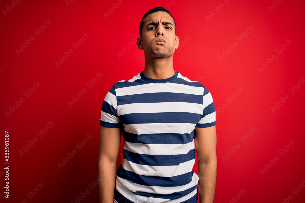 Handsome african american man wearing casual striped t-shirt standing over red background puffing cheeks with funny face. Mouth inflated with air, crazy expression. Handsome african american man wearing casual striped t-shirt standing over red background puffing cheeks with funny face. Mouth inflated with air, crazy expression.