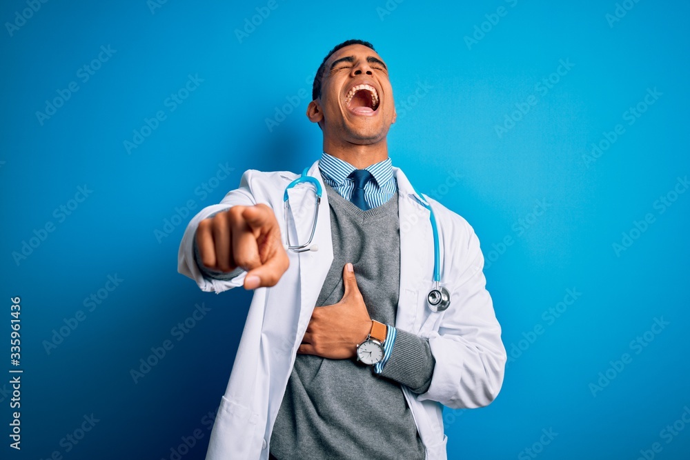 Handsome african american doctor man wearing coat and stethoscope over blue background laughing at you, pointing finger to the camera with hand over body, shame expression Handsome african american doctor man wearing coat and stethoscope over blue background laughing at you, pointing finger to the camera with hand over body, shame expression