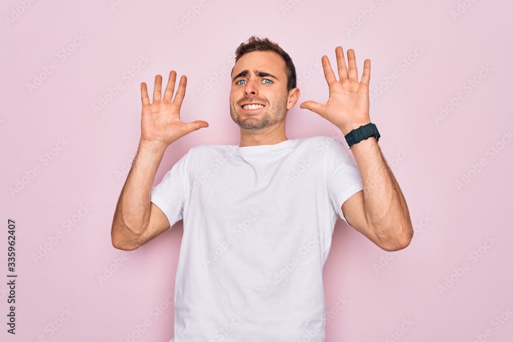 Fototapeta premium Handsome man with blue eyes wearing casual white t-shirt standing over pink background afraid and terrified with fear expression stop gesture with hands, shouting in shock. Panic concept.