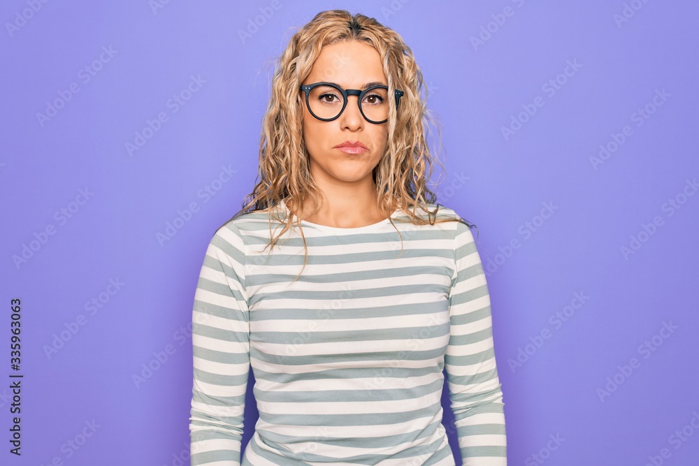 Beautiful blonde woman wearing casual striped t-shirt and glasses over purple background looking sleepy and tired, exhausted for fatigue and hangover, lazy eyes in the morning. Beautiful blonde woman wearing casual striped t-shirt and glasses over purple background looking sleepy and tired, exhausted for fatigue and hangover, lazy eyes in the morning.