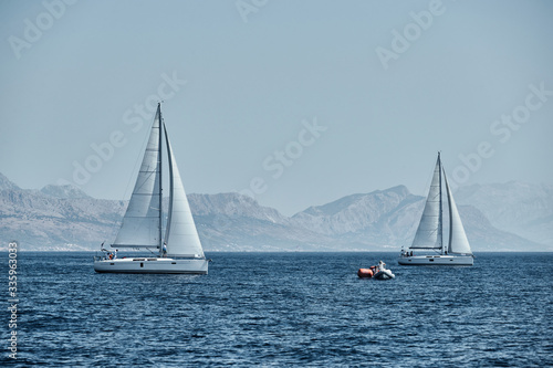 The rubber boat of organizers of a regatta with the judge and balloon of orange color, The race of sailboats, Intense competition, island with windmills are on background