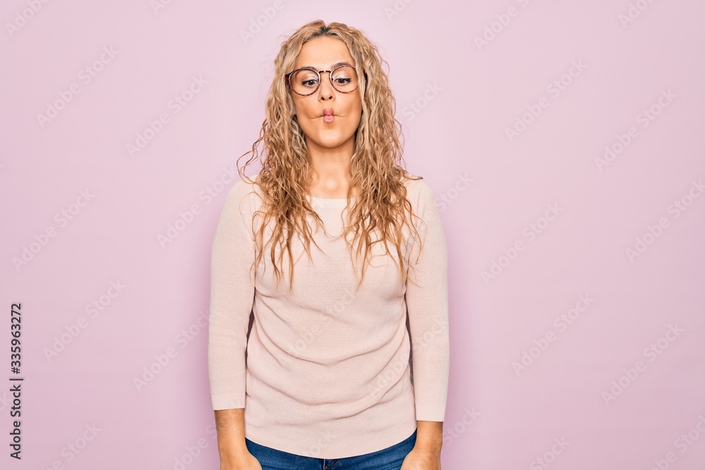 Obraz premium Young beautiful blonde woman wearing casual sweater and glasses over pink background making fish face with lips, crazy and comical gesture. Funny expression.
