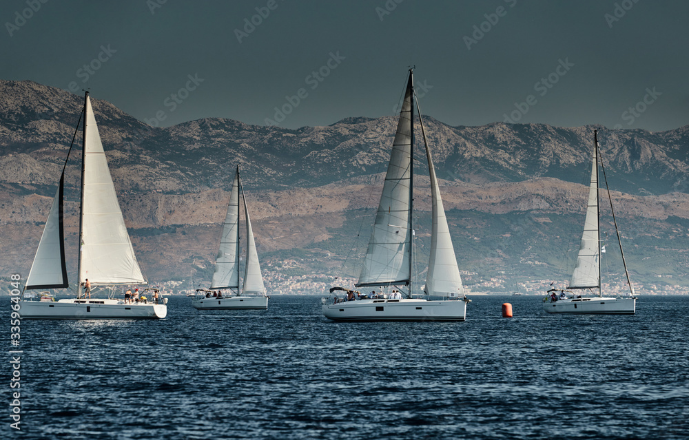 The race of sailboats, a regatta, reflection of sails on water, Intense competition, number of boat is on aft boats, bright colors, island with windmills are on background