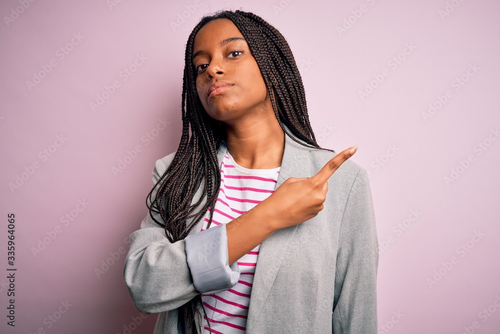 Young african american business woman standing over pink isolated background Pointing with hand finger to the side showing advertisement, serious and calm face Young african american business woman standing over pink isolated background Pointing with hand finger to the side showing advertisement, serious and calm face