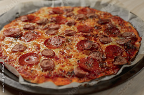 Overhead photography of a homemade pepperoni and sausage pizza on metal tray with a black napkin in a wooden table