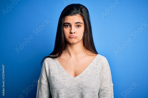 Young beautiful brunette woman wearing casual sweater standing over blue background depressed and worry for distress, crying angry and afraid. Sad expression.