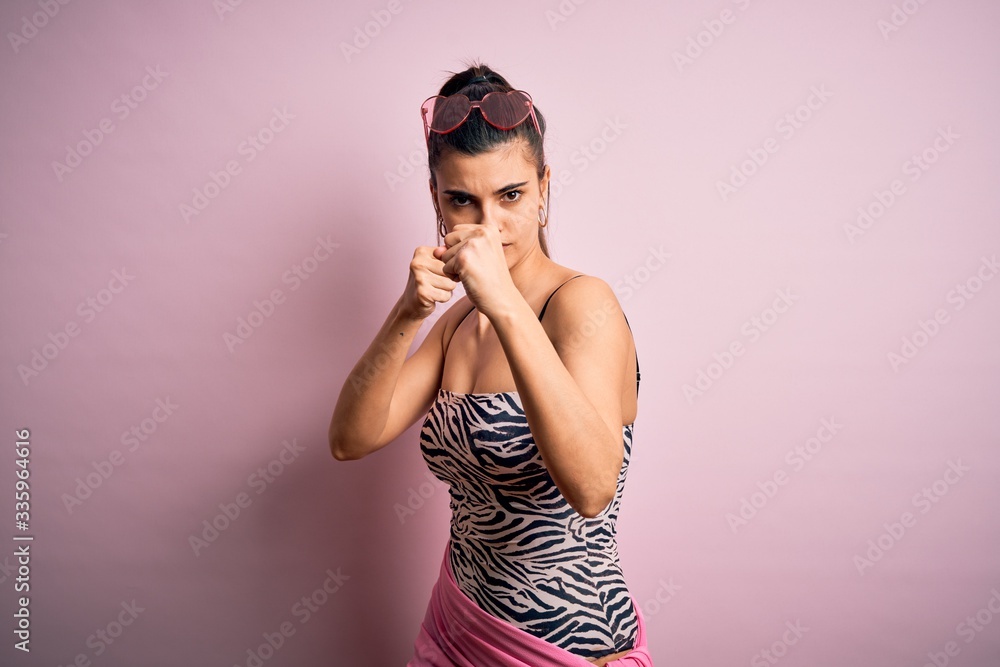 Young beautiful brunette woman on vacation wearing swimsuit over pink background Ready to fight with fist defense gesture, angry and upset face, afraid of problem Young beautiful brunette woman on vacation wearing swimsuit over pink background Ready to fight with fist defense gesture, angry and upset face, afraid of problem