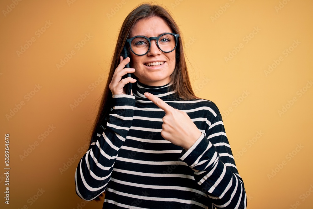 Young beautiful woman with blue eyes having conversation talking on the smartphone very happy pointing with hand and finger Young beautiful woman with blue eyes having conversation talking on the smartphone very happy pointing with hand and finger