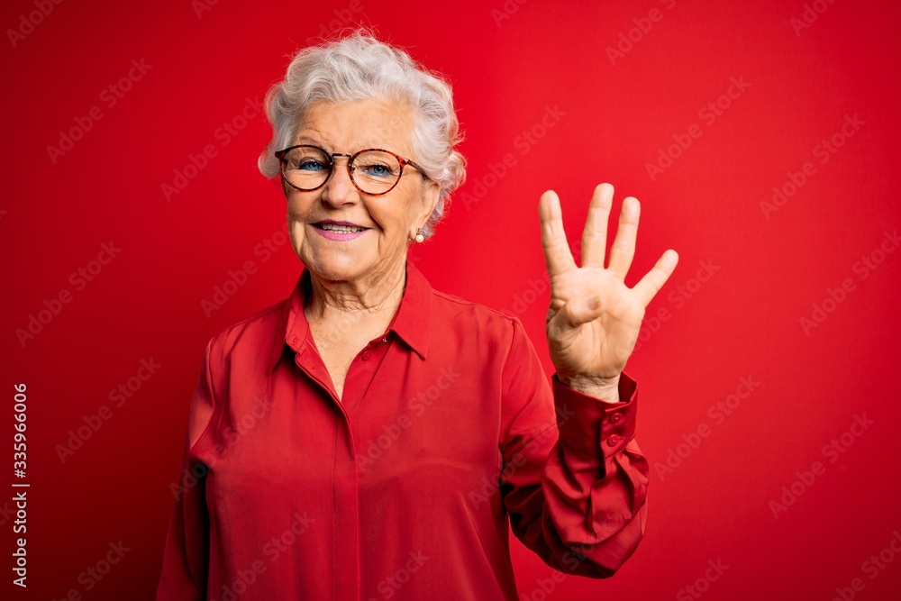 Senior beautiful grey-haired woman wearing casual shirt and glasses over red background showing and pointing up with fingers number four while smiling confident and happy. Senior beautiful grey-haired woman wearing casual shirt and glasses over red background showing and pointing up with fingers number four while smiling confident and happy.