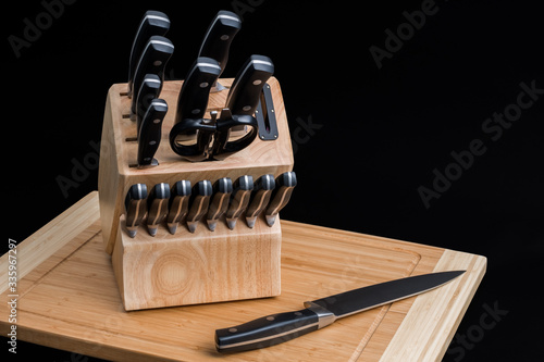 Set of Kitchen knives in a knife block with the chef knife laying on a cutting board, isolated on a black background photo