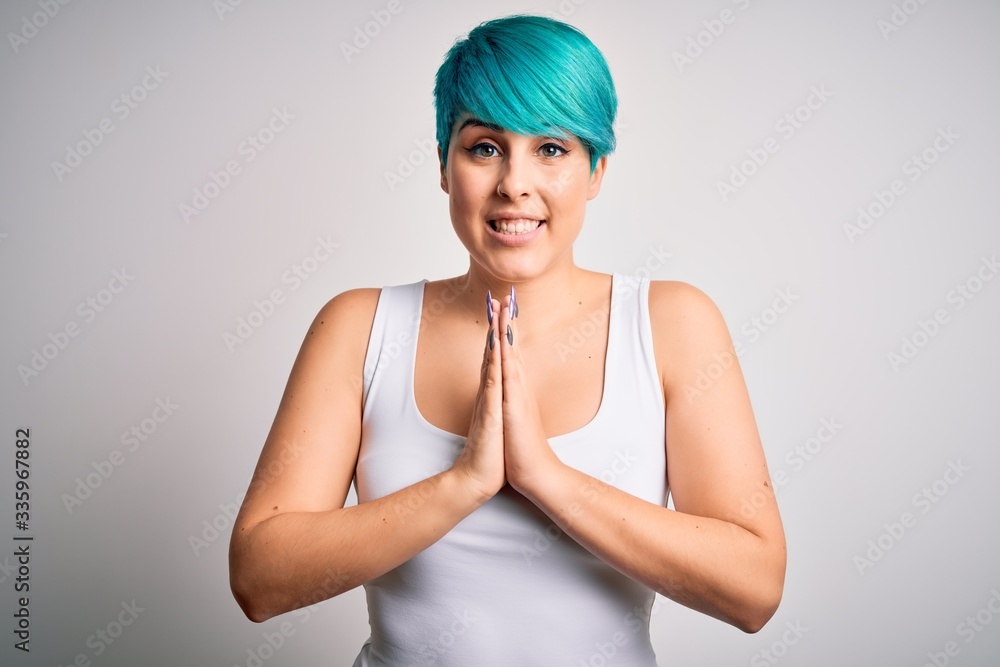 Young beautiful woman with blue fashion hair wearing casual t-shirt over white background praying with hands together asking for forgiveness smiling confident. Young beautiful woman with blue fashion hair wearing casual t-shirt over white background praying with hands together asking for forgiveness smiling confident.