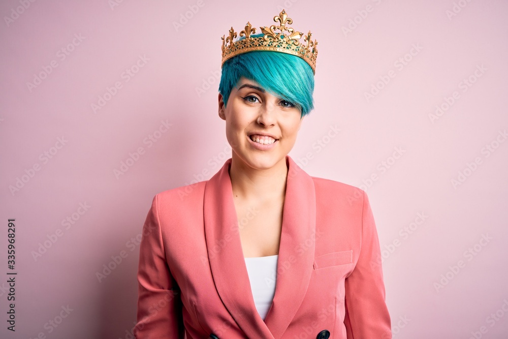 Young business woman with blue fashion hair wearing queen crown over pink isolated background with a happy and cool smile on face. Lucky person.