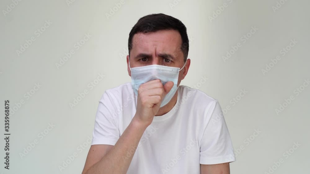 Sick European young man in medical mask coughing up his fist, in front of camera, close-up of face. Concept of Coronavirus COVID-19 Pandemic. Studio shot on isolated white background Sick European young man in medical mask coughing up his fist, in front of camera, close-up of face. Concept of Coronavirus COVID-19 Pandemic. Studio shot on isolated white background