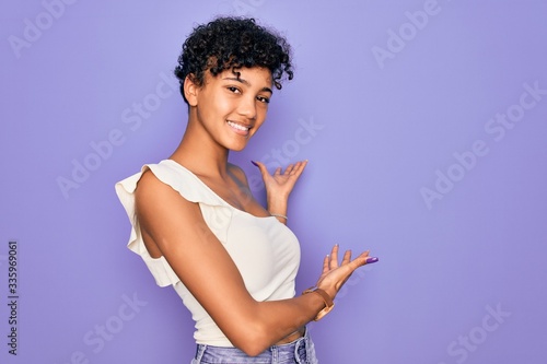 Young beautiful african american afro woman wearing casual t-shirt over purple background Inviting to enter smiling natural with open hand