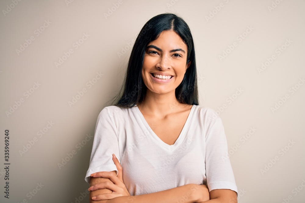 Young beautiful hispanic woman wearing casual white t-shirt over isolated background happy face smiling with crossed arms looking at the camera. Positive person. Young beautiful hispanic woman wearing casual white t-shirt over isolated background happy face smiling with crossed arms looking at the camera. Positive person.