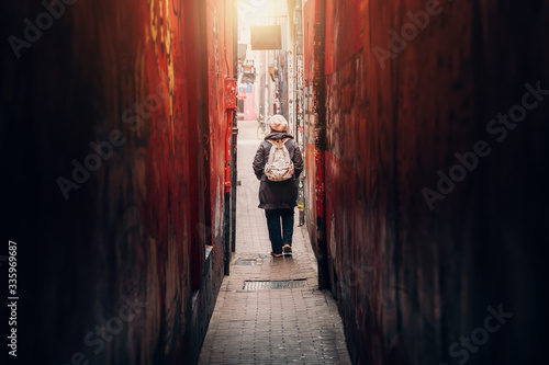 Photography Traveler girl leaves narrow long red corridor or tunnel on city street, rear view