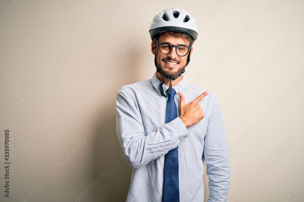 Young businessman wearing glasses and bike helmet standing over isolated white bakground cheerful with a smile of face pointing with hand and finger up to the side with happy and natural expression 