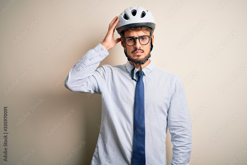 Young businessman wearing glasses and bike helmet standing over isolated white bakground confuse and wonder about question. Uncertain with doubt, thinking with hand on head. Pensive concept. Young businessman wearing glasses and bike helmet standing over isolated white bakground confuse and wonder about question. Uncertain with doubt, thinking with hand on head. Pensive concept.