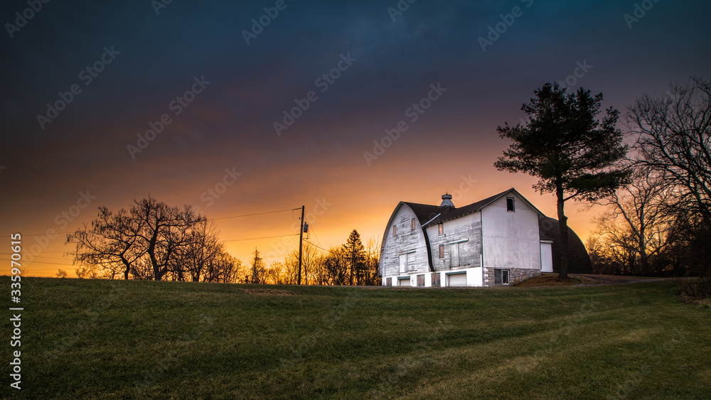 Fototapeta premium Panoramic view of a white barn in a public park beneath a stirring rural sunrise